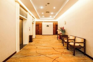 Un pasillo de hotel con alfombra de diseño de piedra, sillas de madera y una recepción.
