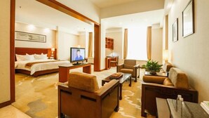Quarto de hotel com cama, televisão, escrivaninha, poltrona e sofá.