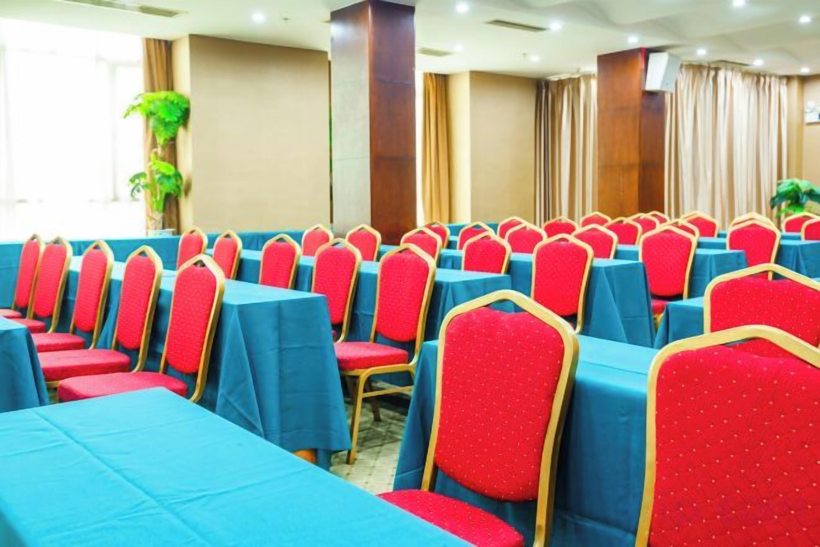 A conference room with rows of tables and chairs, large windows, and a plant.