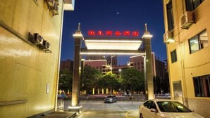 Entrada de hotel com um letreiro iluminado em destaque, área de estacionamento e edifícios ao redor.