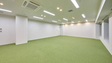 A spacious room with a green carpet, white walls, and ceiling lights.