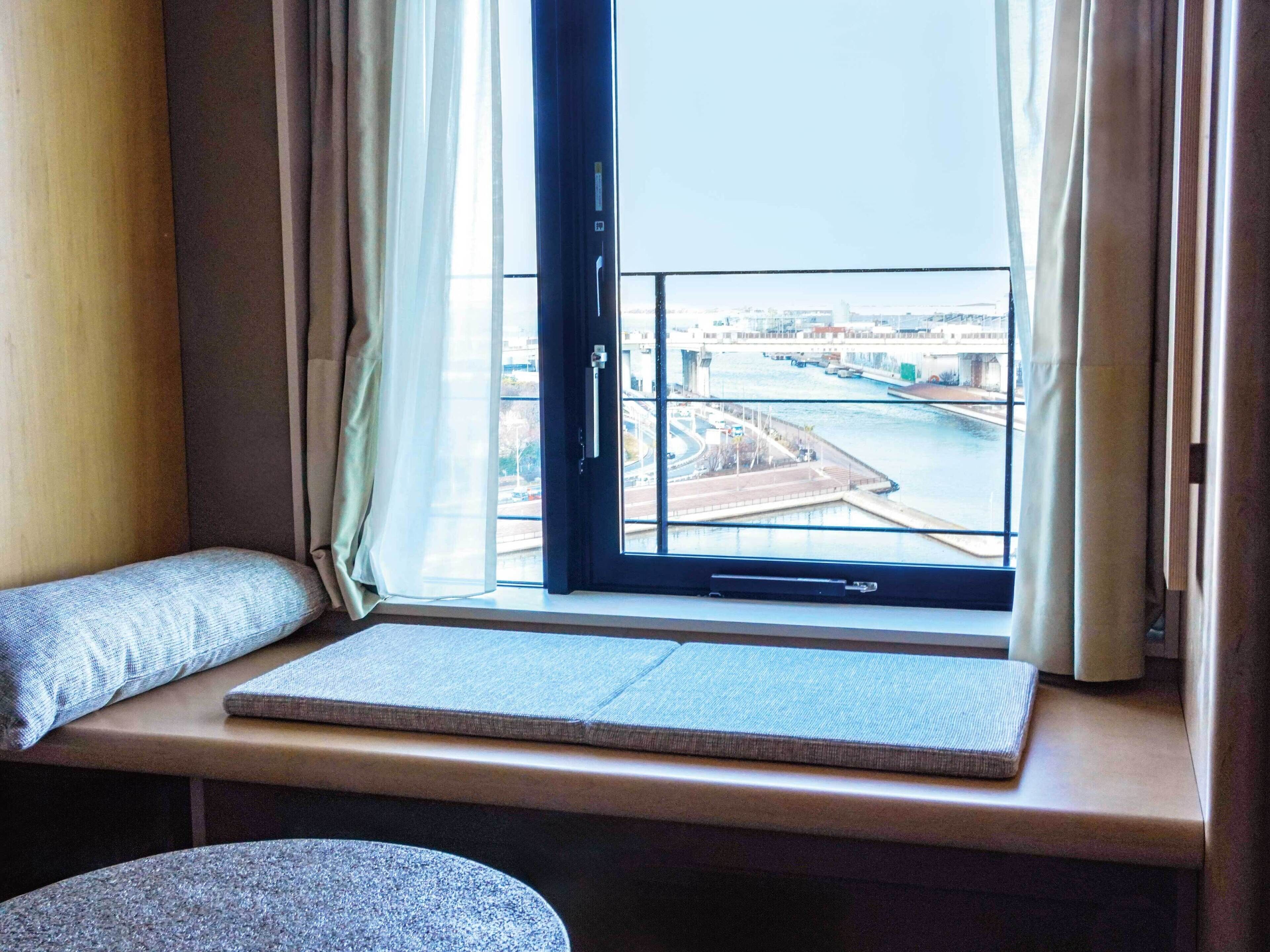 A window seat with a view of a river and bridges, a cushion, and a small table.