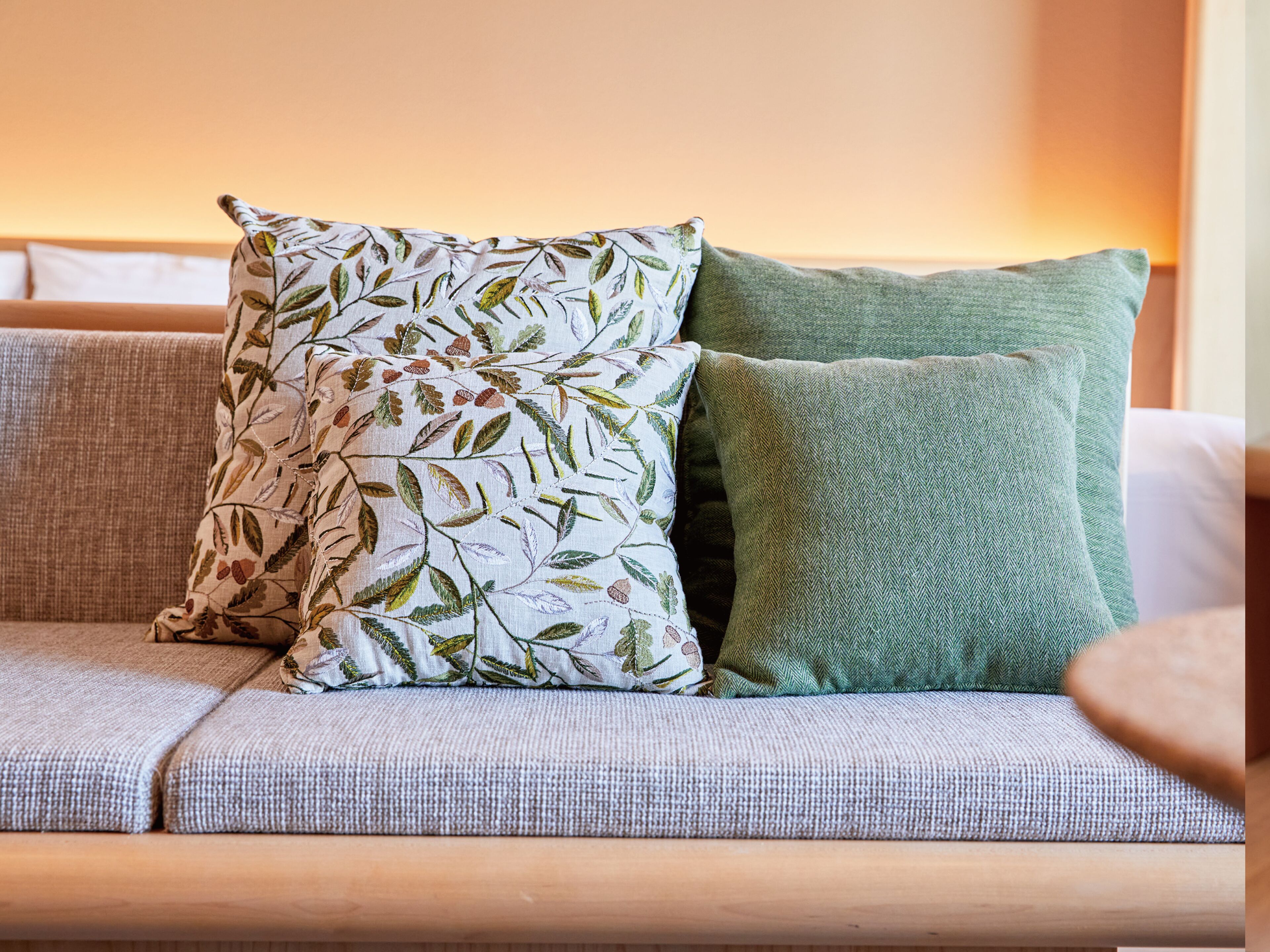 Ein Sofa mit zwei Kissen, eines mit Blattmuster und das andere schlicht grün.