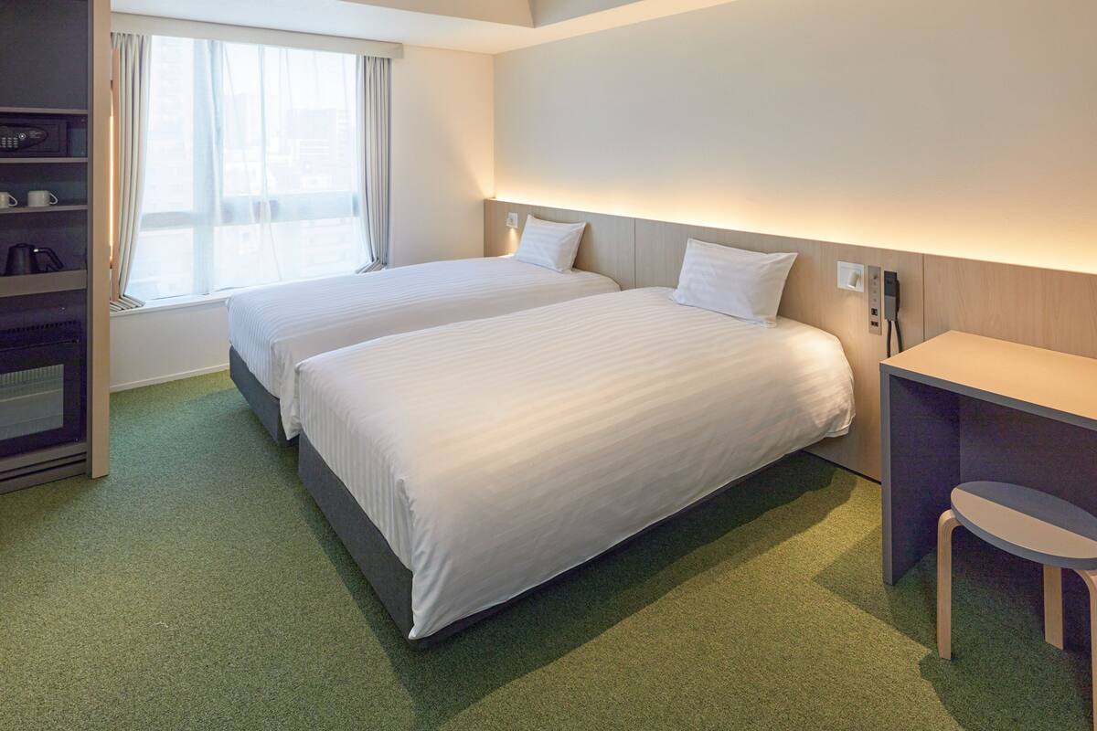 Habitación de hotel con dos camas, un escritorio, una silla, microondas y ventana con cortinas.