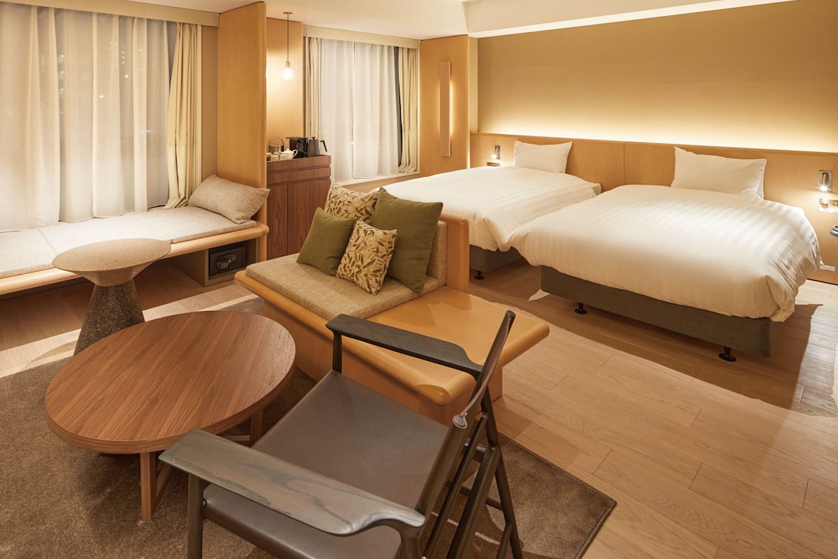 Habitación de hotel con sofá, dos camas, una mesa de comedor y una pequeña cocina.