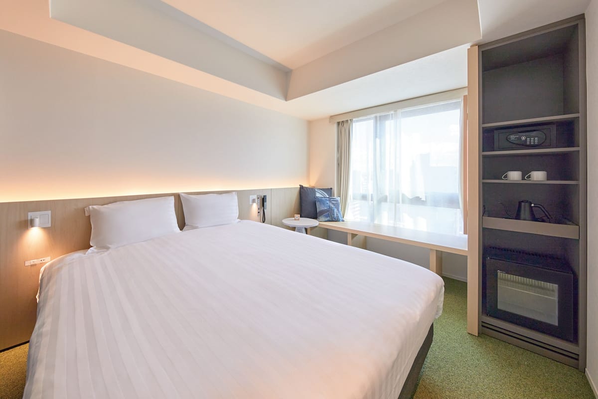Habitación de hotel con una cama grande, una mesita pequeña, un banco, un televisor y un horno empotrado.