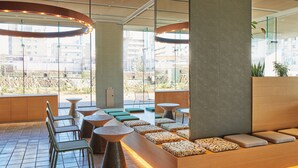 Un espace de détente moderne, doté de différents types de sièges, d’une colonne centrale et de grandes fenêtres offrant une vue sur le paysage urbain.