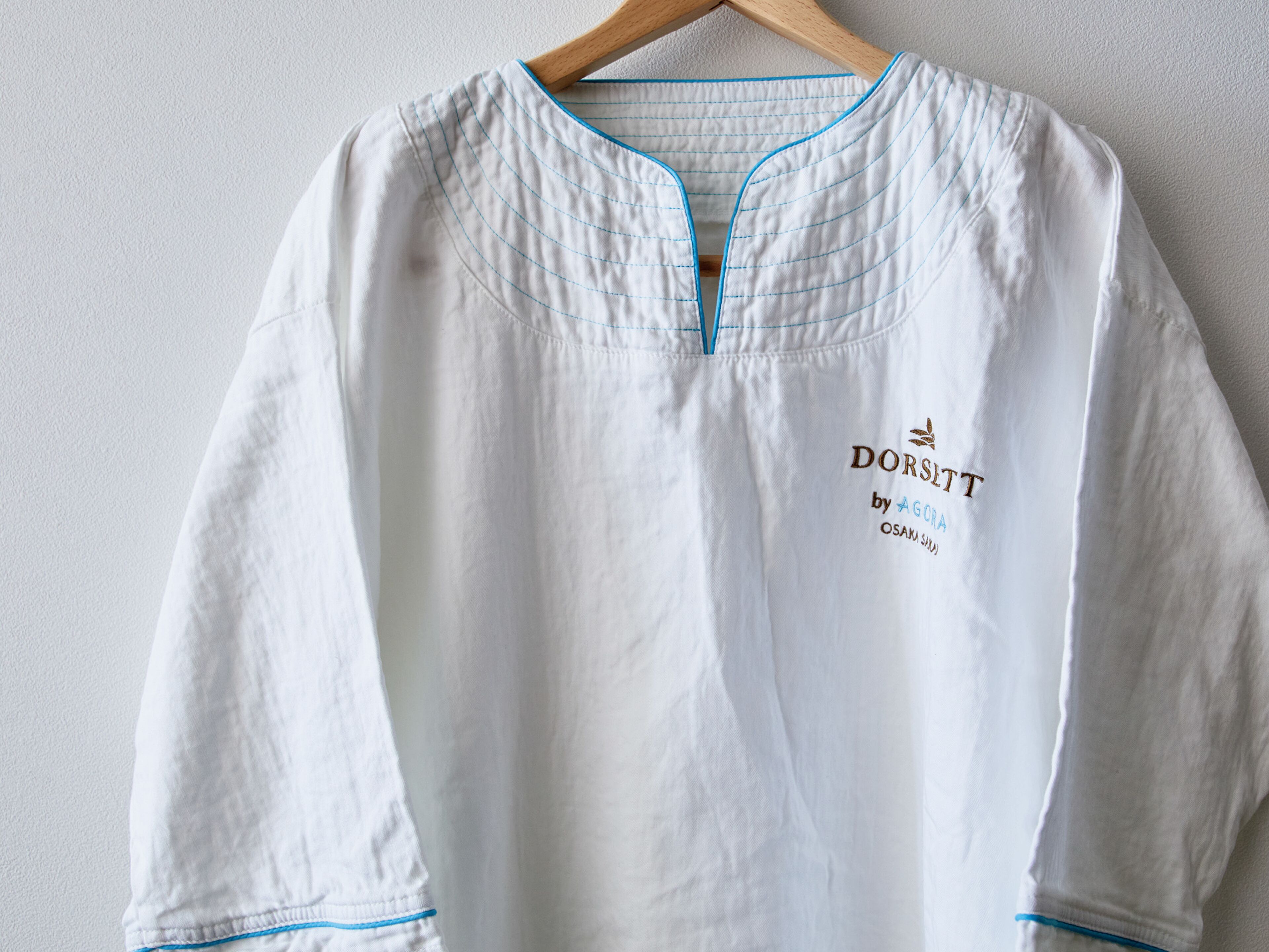 Uma camisa branca de manga comprida com detalhes azuis e texto bordado na frente.
