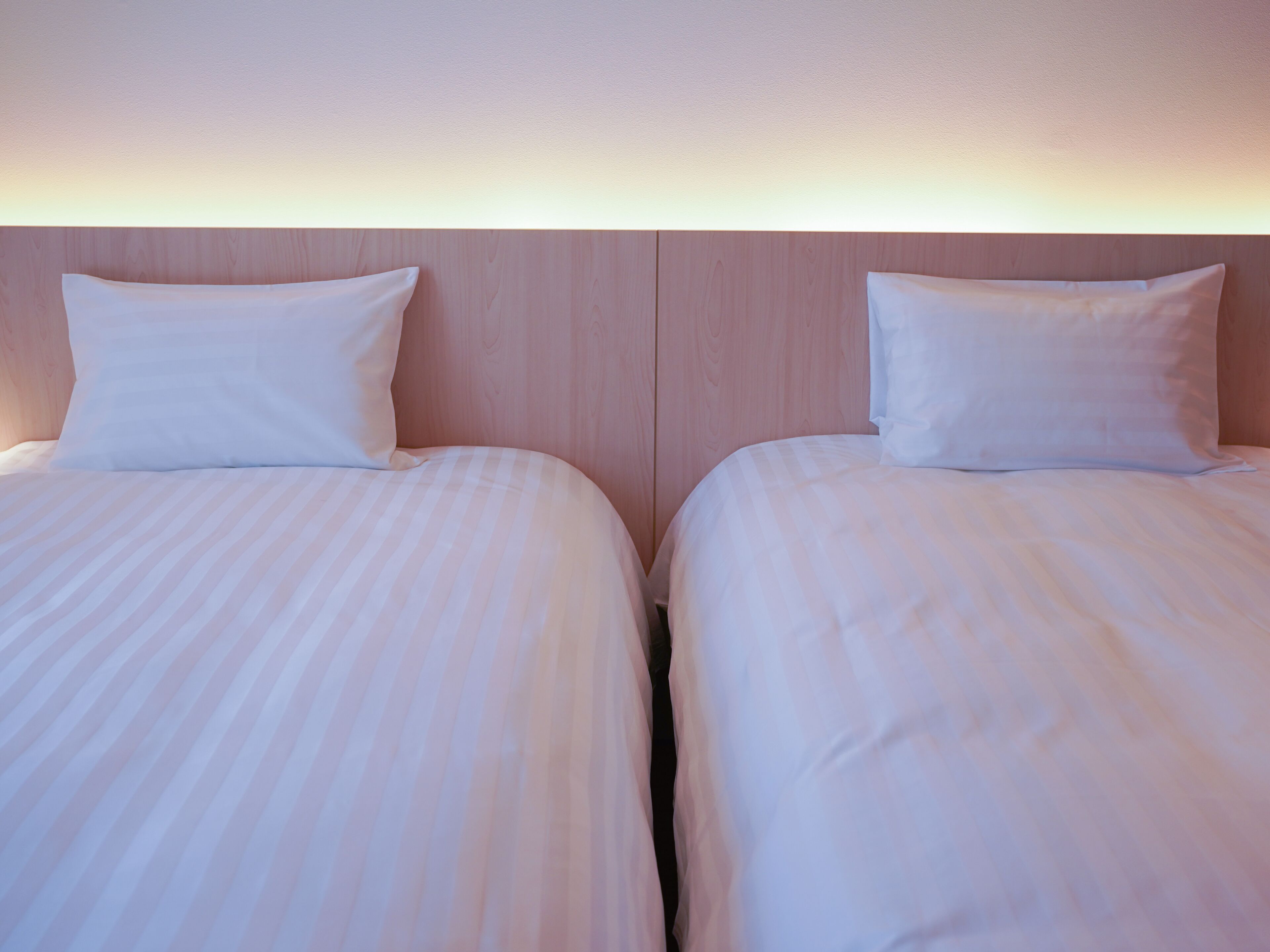 Two adjacent beds with white linens and wooden headboards in a hotel room.