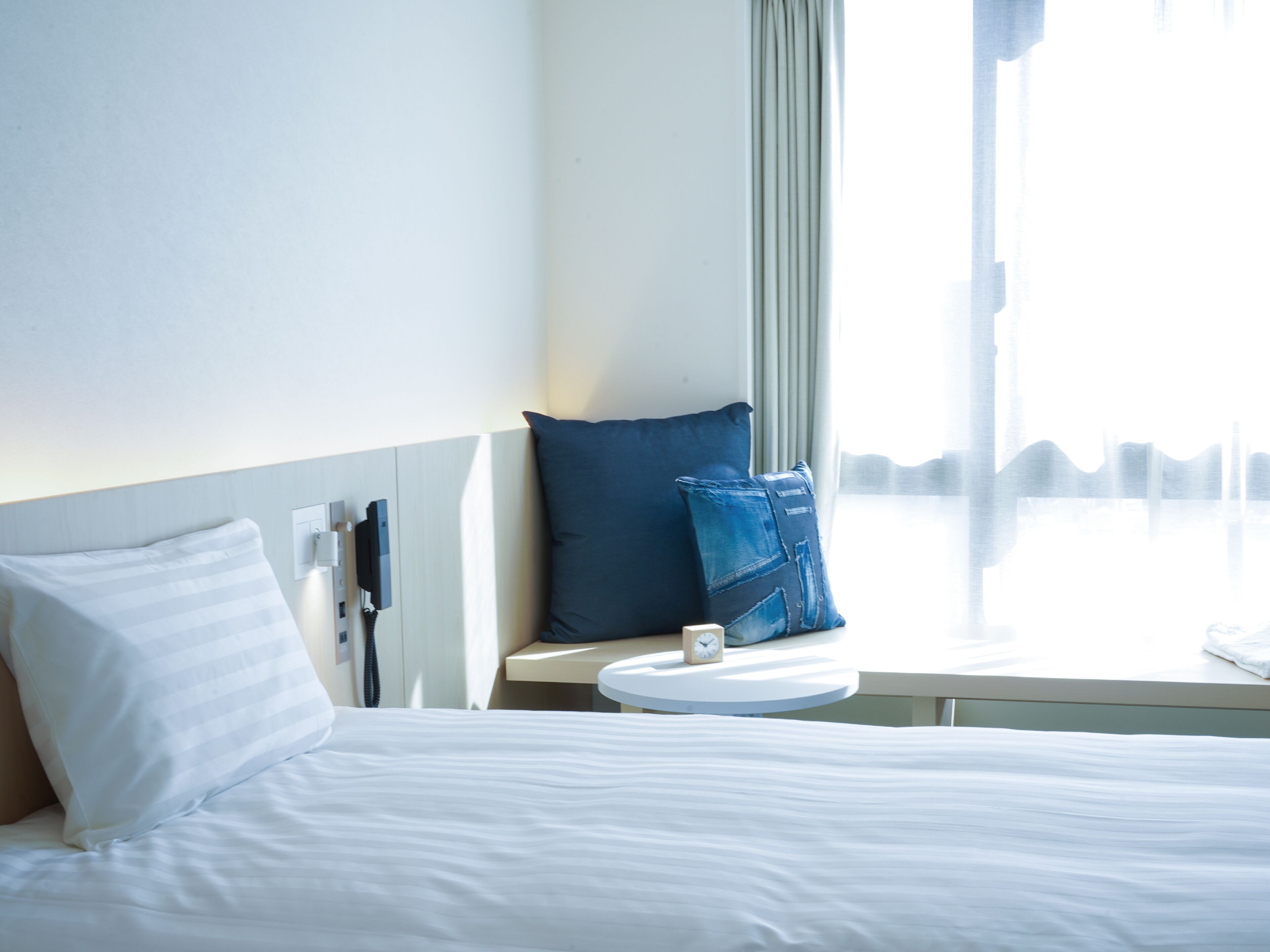 A hotel room with a bed, a bedside table with a clock, and a window with a view of the city skyline.
