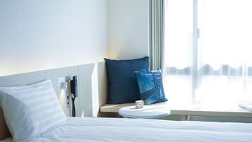A hotel room with a bed, a bedside table with a clock, and a window with a view of the city skyline.