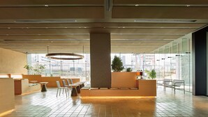 Eine geräumige Lobby mit modernem Design, ausgestattet mit einer zentralen Sitzecke, einer großen Hängeleuchte und Blick auf die Stadt durch große Fenster.