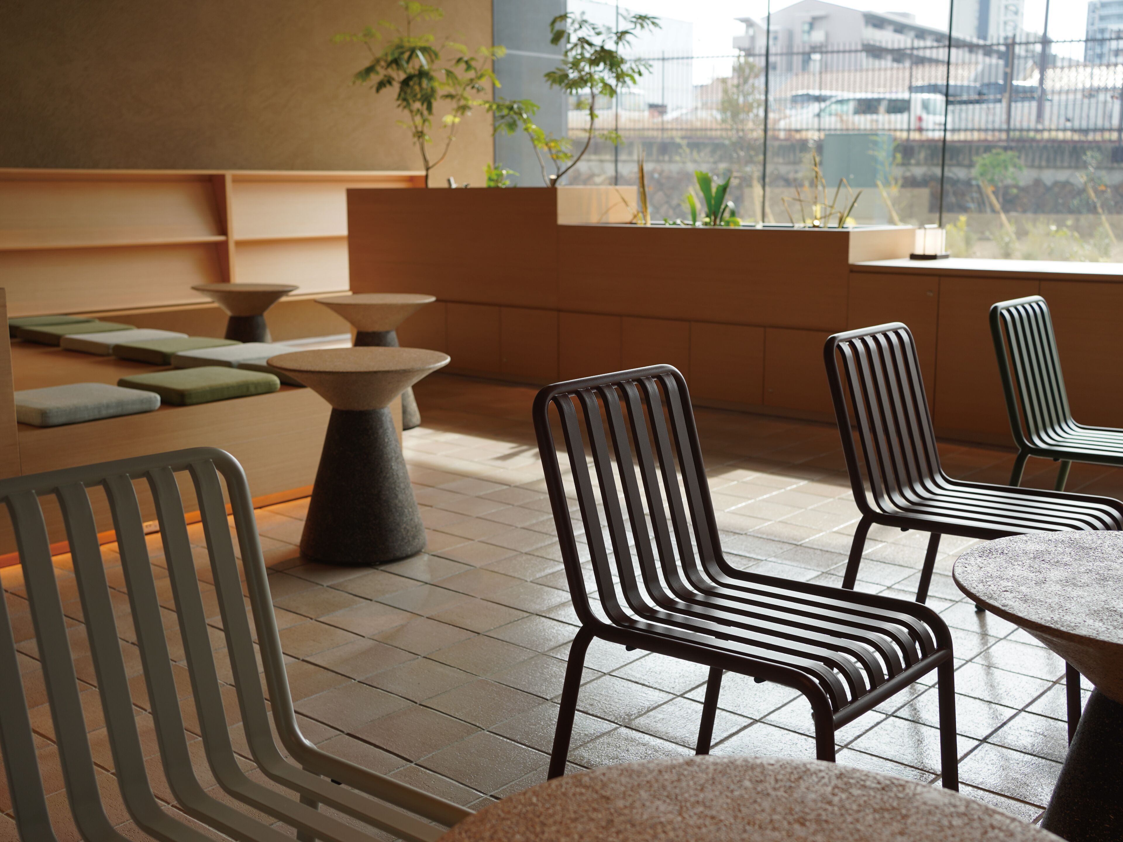 A modern outdoor seating area with tiered tables and chairs, a view of the cityscape through a window, and potted plants.