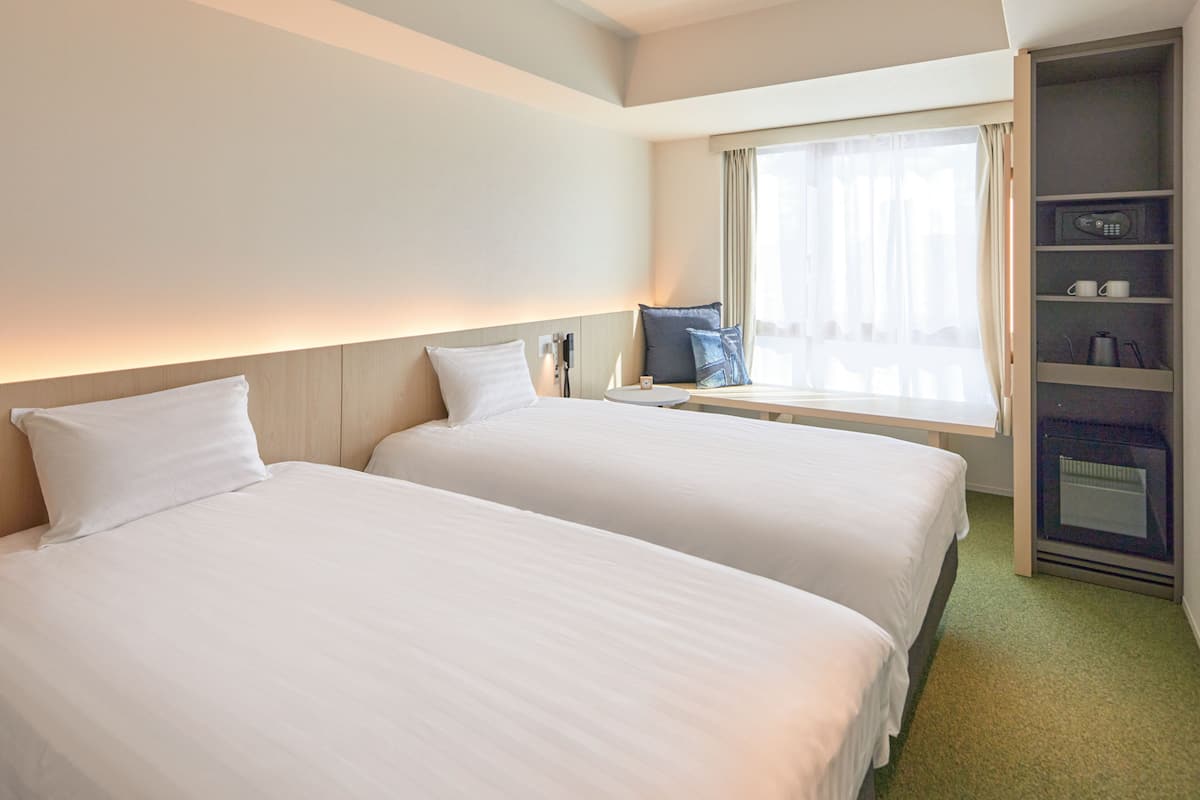 Habitación de hotel con dos camas, una ventana con cortinas, una mesita de noche y un estante con microondas integrado.