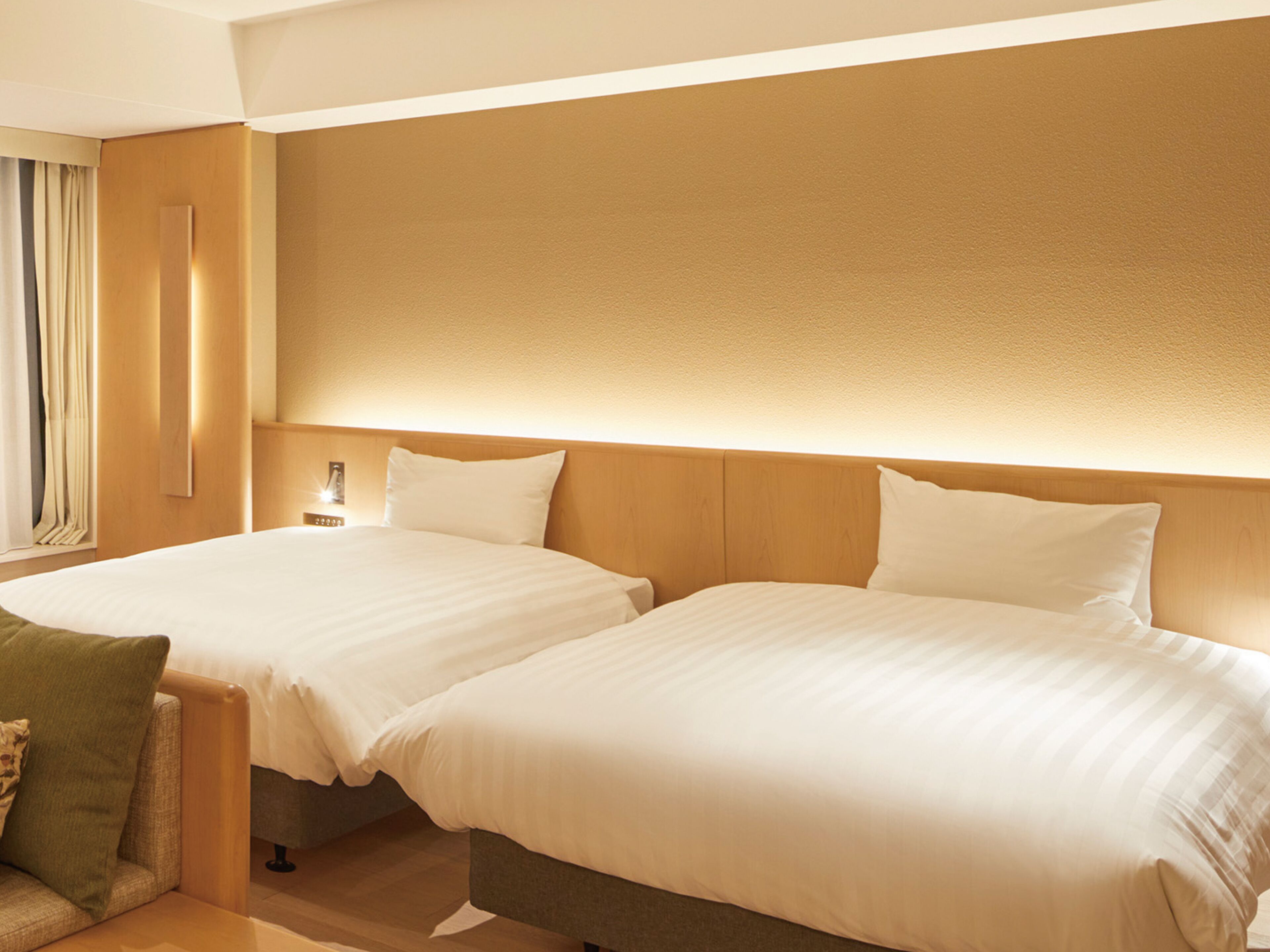 A hotel room with two beds, a wooden headboard, a nightstand, and a green armchair.
