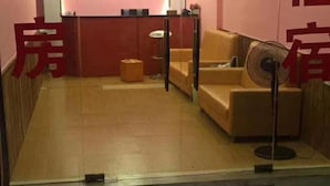 A hotel room with a wooden floor, a sofa, a standing fan, and a small table. - Youranju Inn (Xiamen)