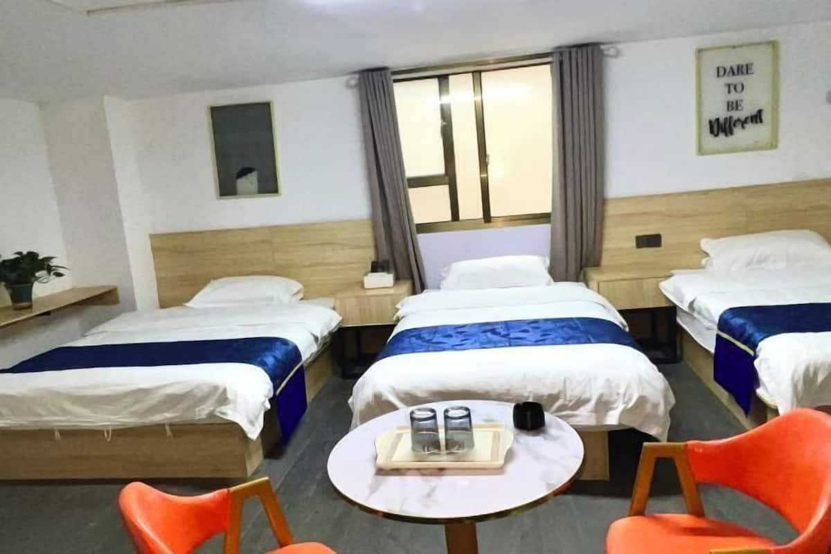 A hotel room with four single beds, a small round table with a tray of glasses and a cup, and two orange chairs.