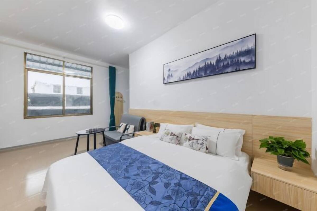 A hotel room with a bed, a desk, a chair, a window, and a wall-mounted painting.