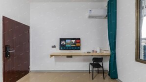 A room with a wooden door, a small desk with a chair, a teal curtain, and a wall-mounted air conditioner. - Youranju Inn (Xiamen)