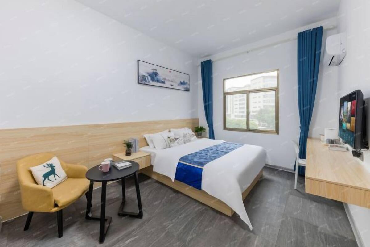 A hotel room with a bed, a desk, a chair, a small table, and a window.