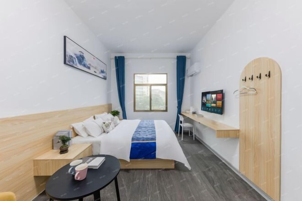 Ein kleines Hotelzimmer mit einem Bett, einem Schreibtisch, einem Stuhl, einem Fernseher und einem Kleiderschrank.