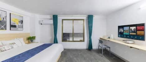 Habitación de hotel con cama, escritorio, silla, ventana con cortinas y televisor montado en la pared.