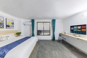 Ein Hotelzimmer mit Bett, Schreibtisch, Sessel, einem Fenster mit Vorhängen und einem an der Wand befestigten Fernseher.