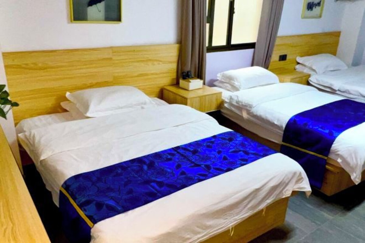 A hotel room with two single beds, wooden headboards, and a small bedside table with a lamp.