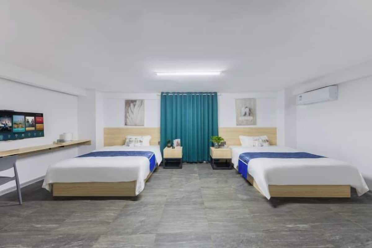 A hotel room with two beds, a desk, a TV, and a window with curtains.