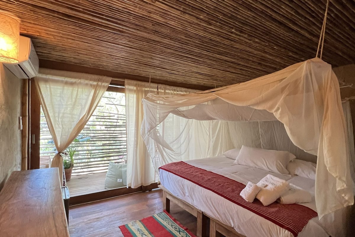 A room with a bed under a canopy, a wooden table, and a window with curtains.