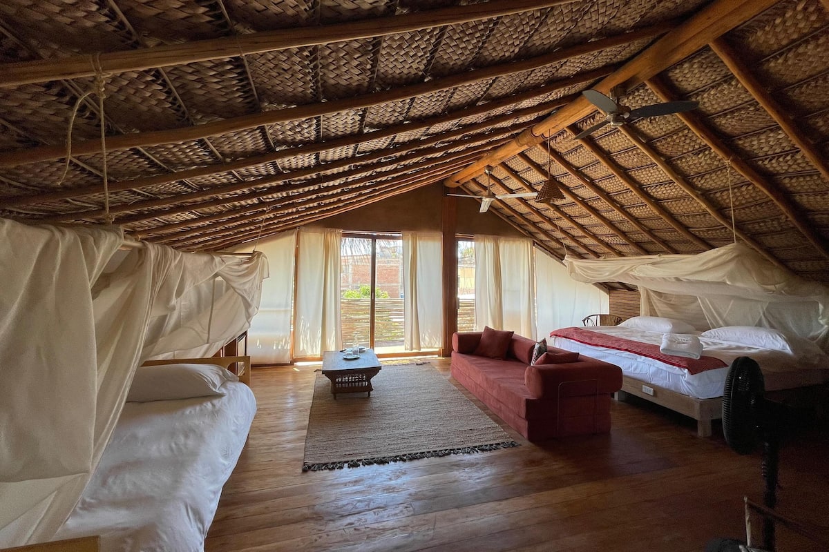 A cozy, high-ceilinged room with a thatched roof, a bed, a sofa, and a small table.