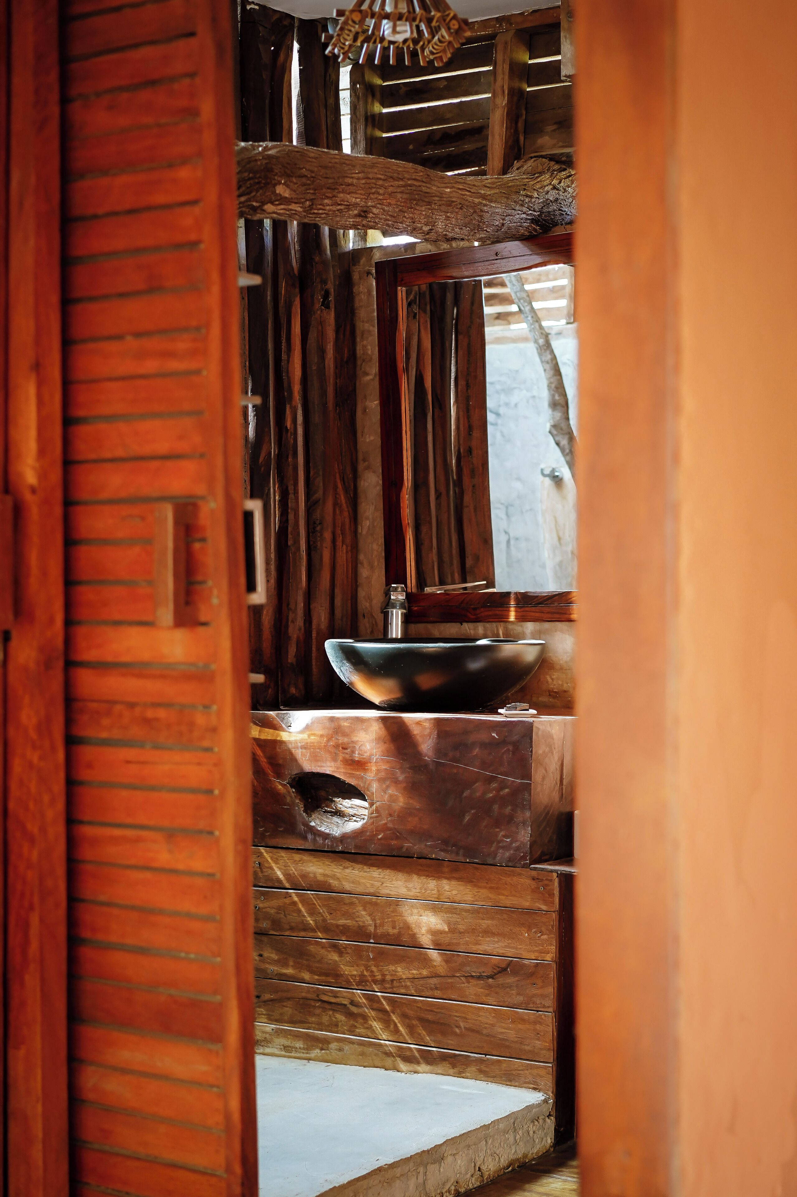 Interior de madera con una estructura grande y rústica de vigas de madera, un lavamanos de metal y un marco de puerta de madera.