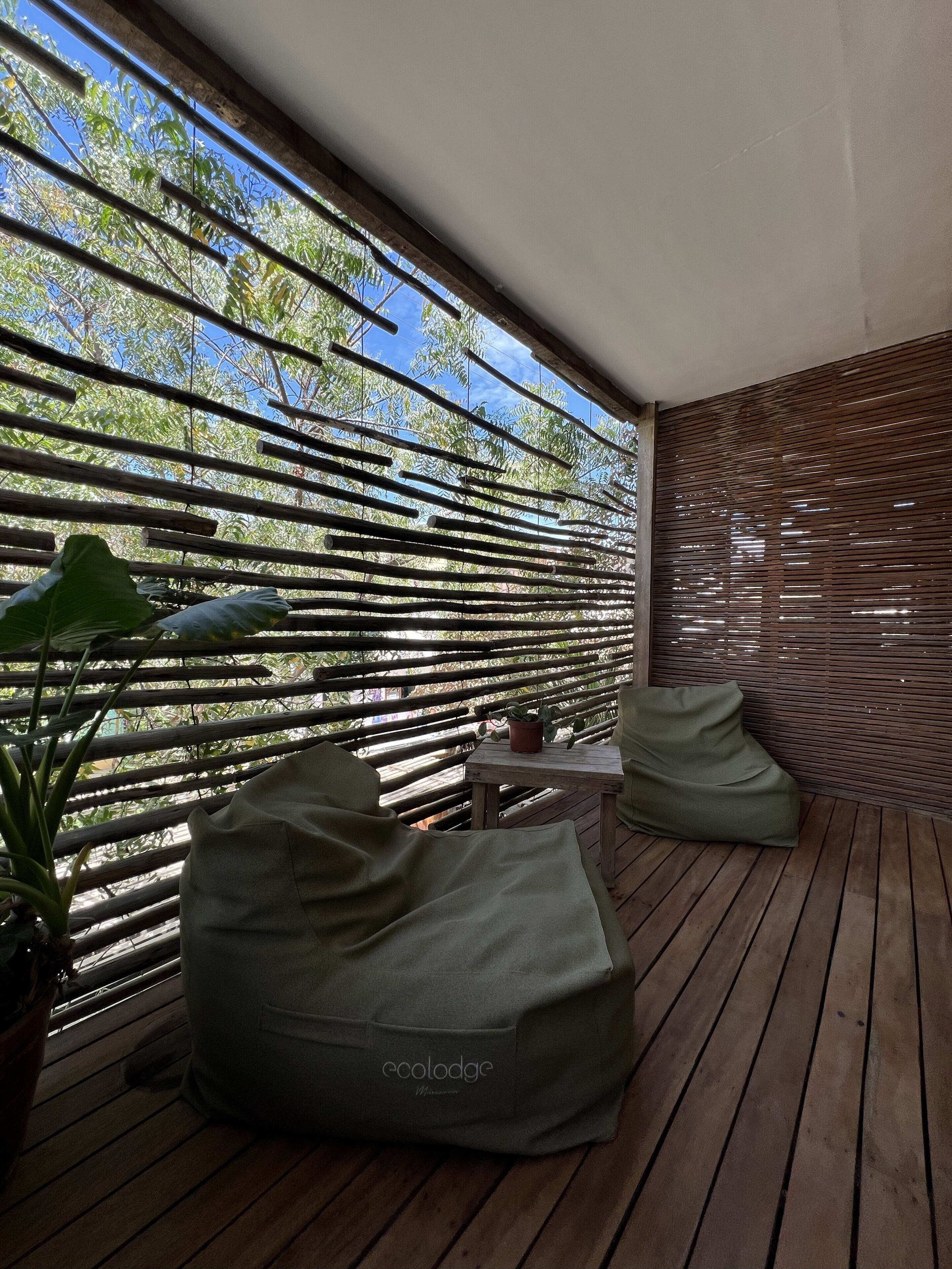 A wooden deck with a green bean bag chair and a small table, surrounded by a bamboo fence and potted plants.
