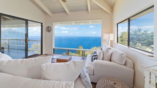 A cozy room with a large window overlooking the sea, a ceiling fan, and a comfortable seating area. - Tranquil Ocean View Cottage: Your Idyllic Escape at Waipio Valley, Big Island HI (Honokaa)