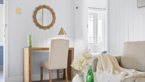 A room with a wooden desk, a chair, a mirror, a lamp, a sofa, and a vase with flowers.