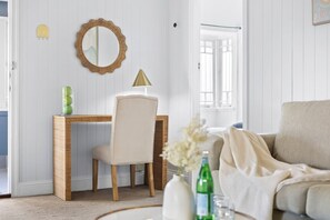 A room with a wooden desk, a chair, a mirror, a lamp, a sofa, and a vase with flowers.