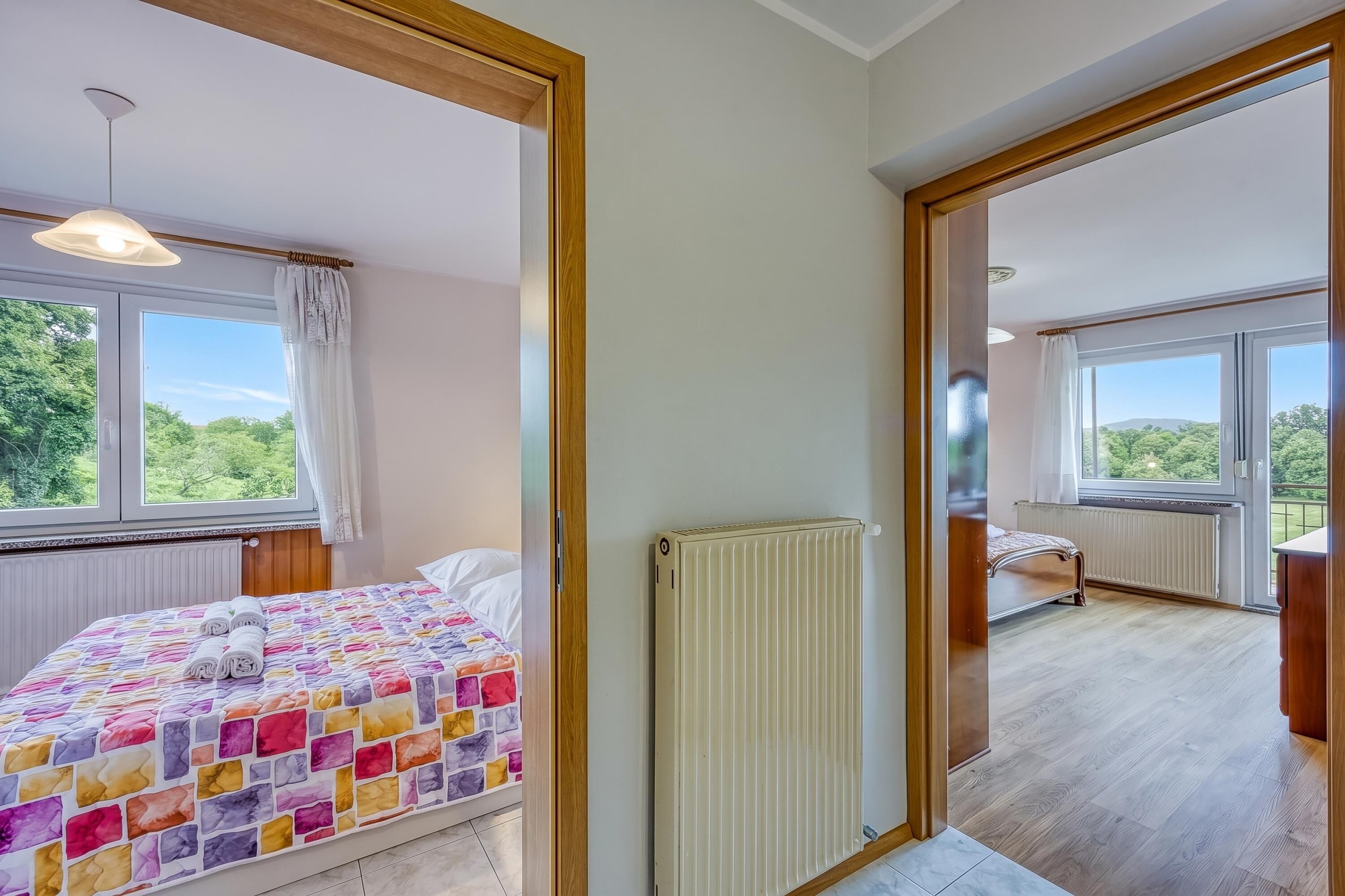 A bedroom with a large window, a radiator, and a bed with a colorful quilt.