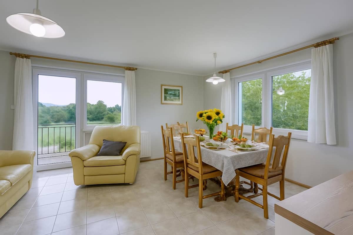 Un coin repas avec une table dressée pour quatre personnes, entourée de chaises en bois, d’un canapé jaune et d’une table à manger recouverte d’une nappe blanche.