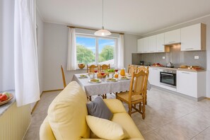 Uma cozinha moderna com armários brancos, uma mesa de jantar posta para quatro pessoas e um sofá em primeiro plano.