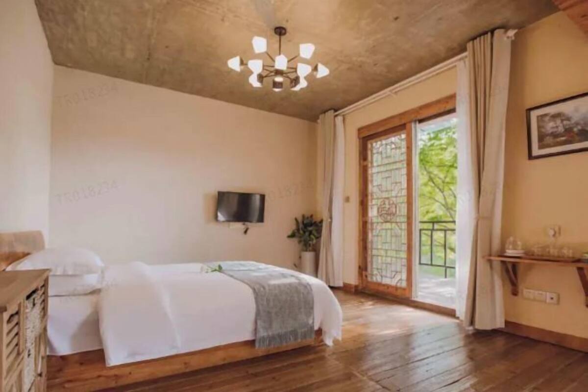 A bedroom with a bed, wooden flooring, a television, and a sliding glass door to the outside.