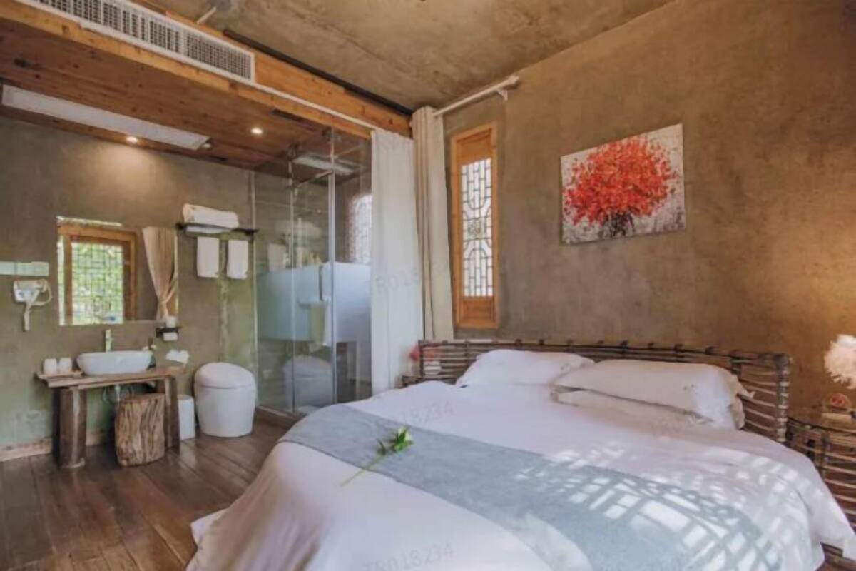 A bedroom with a bed, a bedside table, a window with curtains, and a wall-mounted artwork.