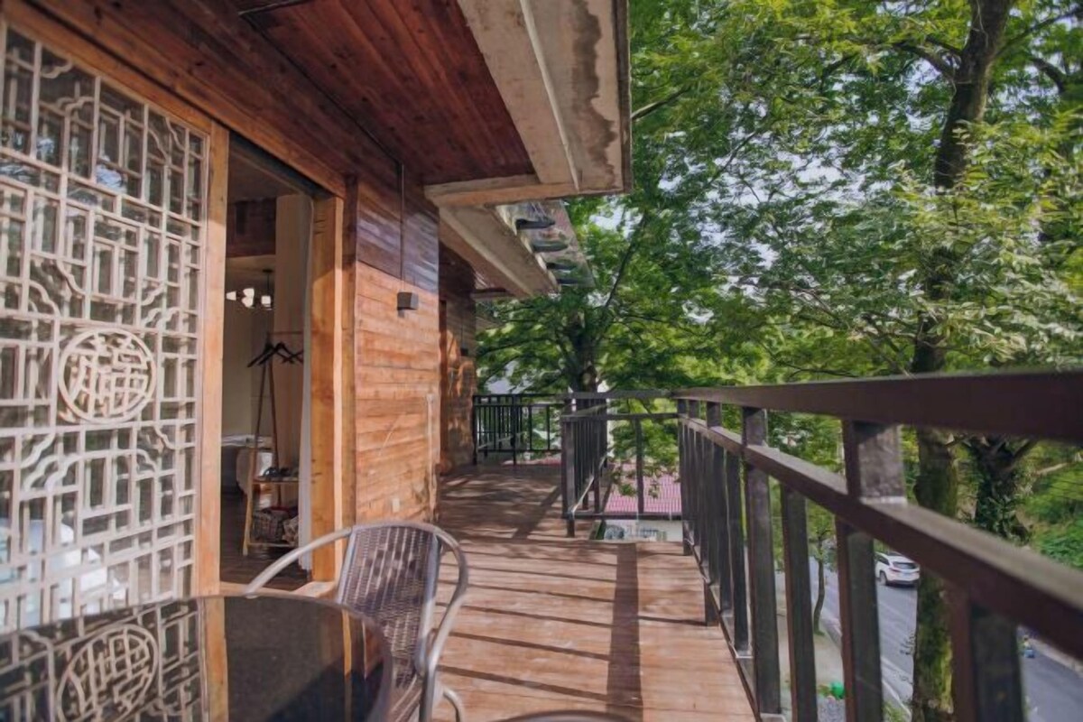A wooden balcony with a metal railing, a chair, and a view of trees and a road.