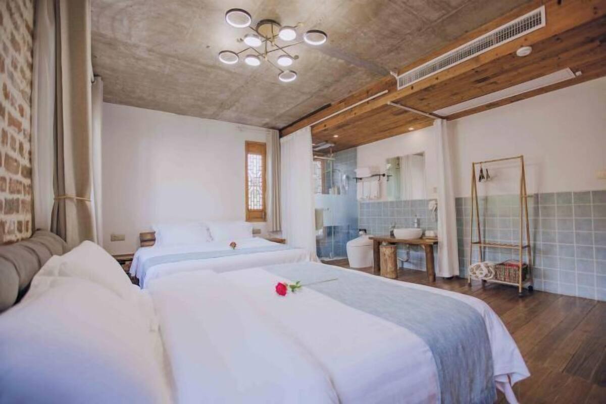 A hotel room with two beds, a wooden ceiling, a bathroom with a sink and mirror, and a small table.
