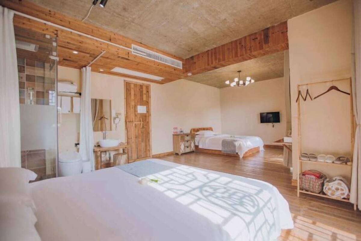 A bedroom with a large bed, a bedside table, a wardrobe, a mirror, a TV, and a shoe rack.