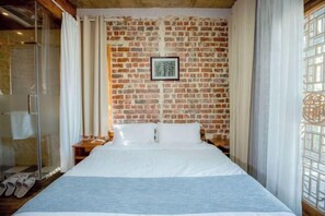 A hotel room with a brick wall, a bed with white linens, a framed picture on the wall, and a window with curtains. - Jushe village Meisu Inn (Deqing)