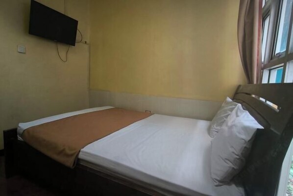 A single bed with a brown blanket, a white pillow, and a headboard. A flat-screen TV is mounted on the wall above the bed. - Hotel Simpang Lima Semarang (South Semarang)