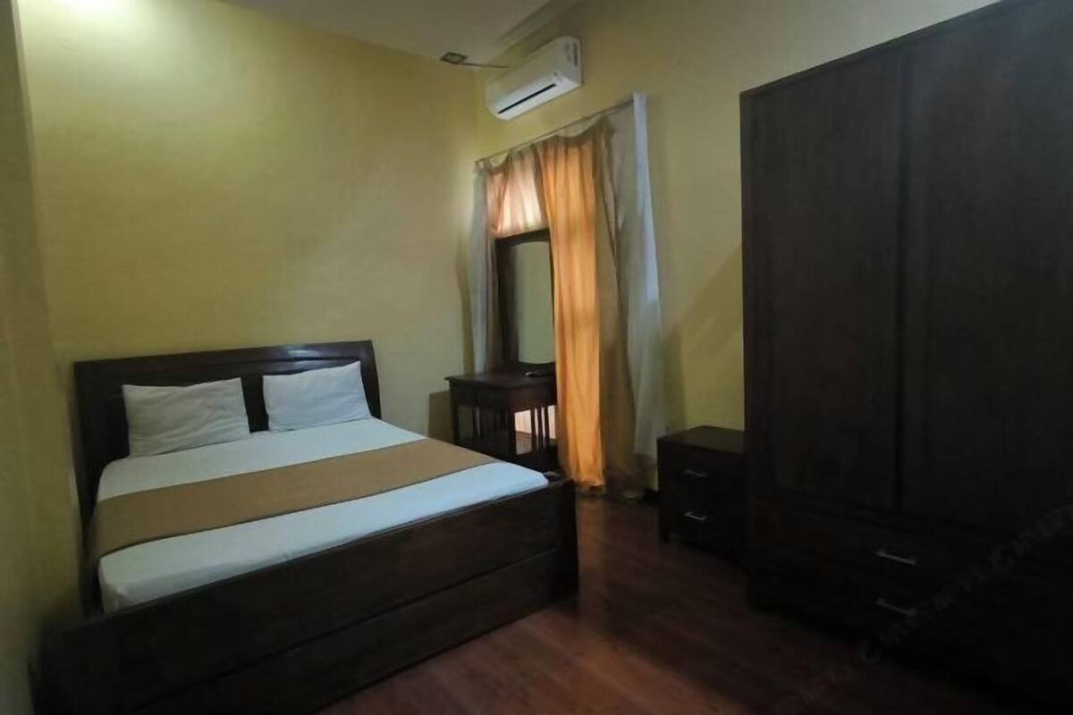 A bedroom with a bed, an air conditioning unit, a wardrobe, and a small table.