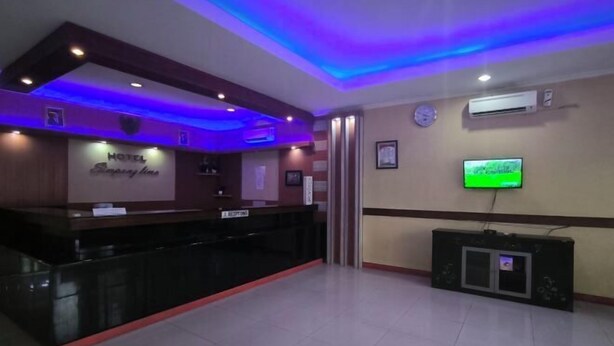 A hotel reception area with a reception desk, a clock, an air conditioning unit, and a television on the wall. - Hotel Simpang Lima Semarang (South Semarang)