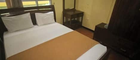 A bed with white bedding and a brown accent, a small wooden nightstand, a mirror, and a window with a view.