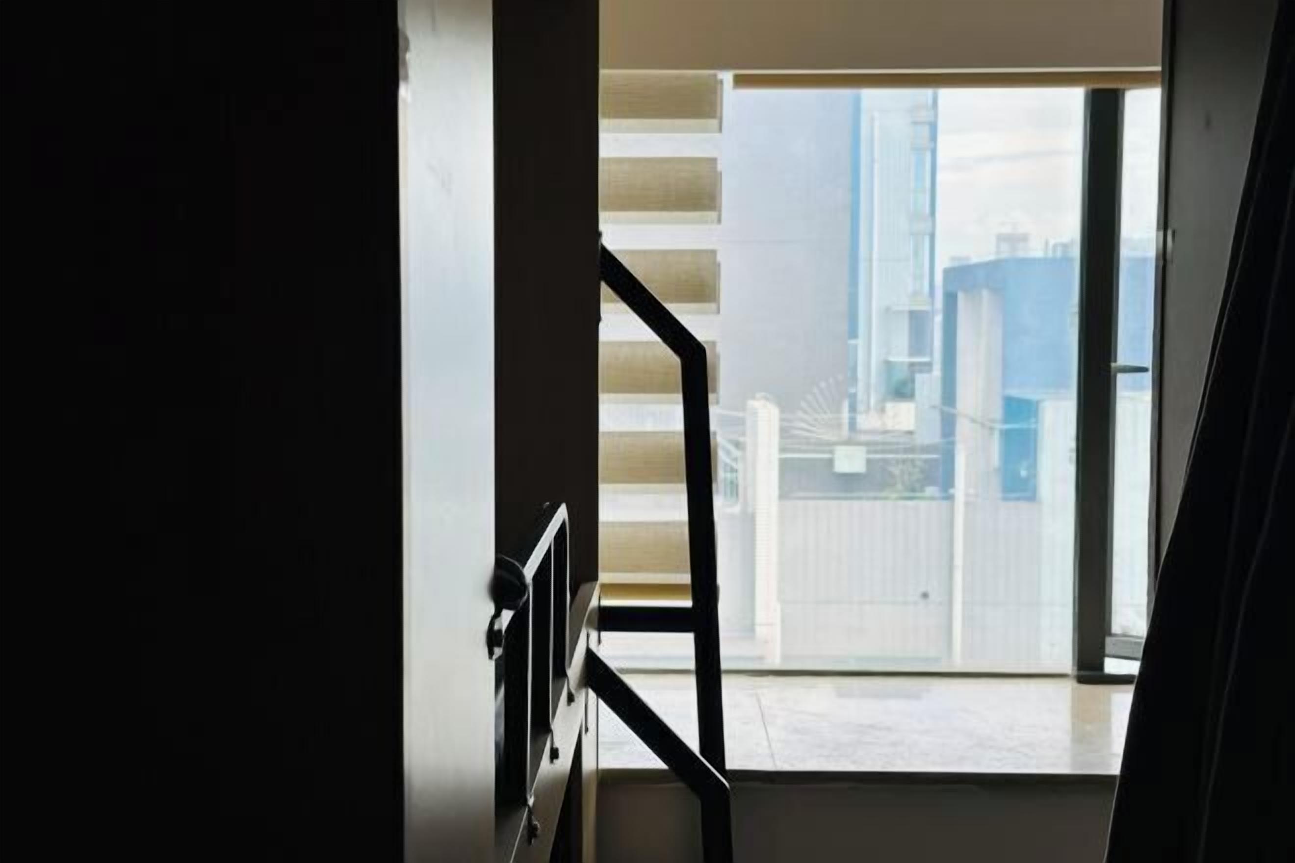 A view from a window with a metal railing, looking out onto a cityscape with buildings and a clear sky.
